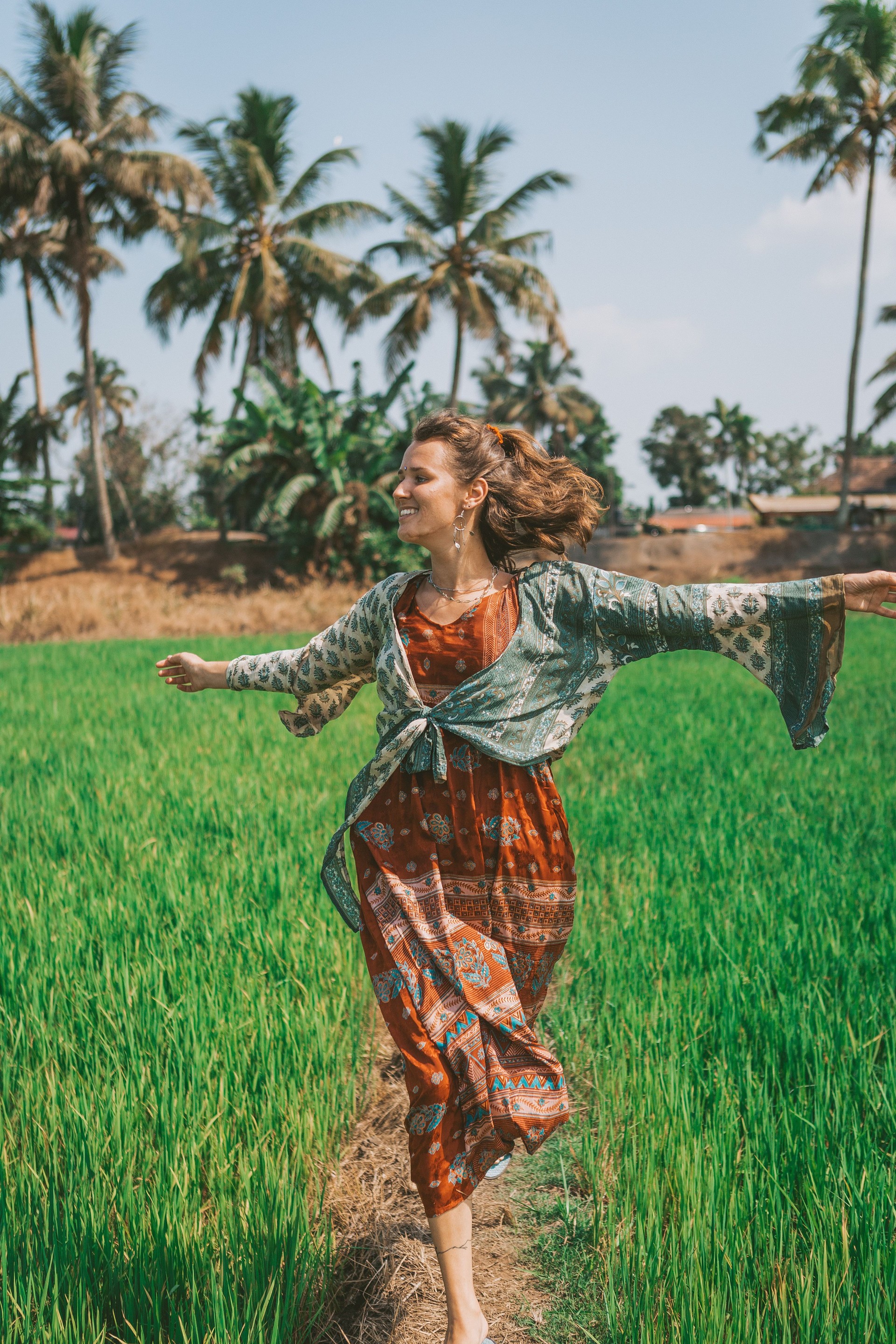 women is running on a rice field in a red dress, with palmtrees in the background